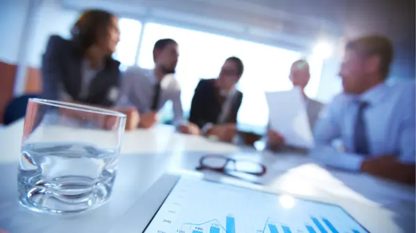 Réunion d'équipe floue en arrière-plan avec un verre d'eau et une tablette au premier plan.