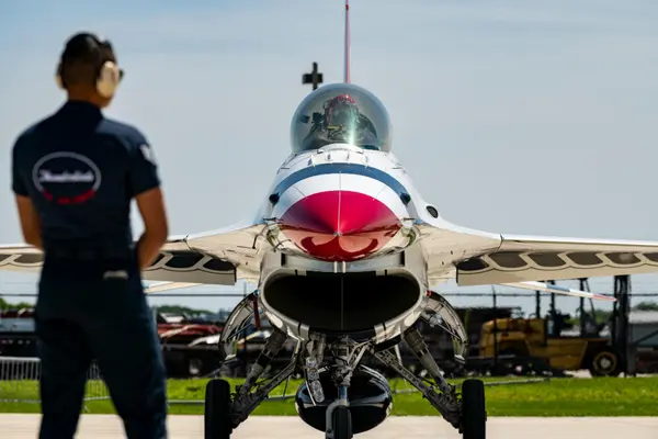 Vue frontale d'un avion de chasse blanc, rouge et bleu sur une piste, avec un technicien de dos.