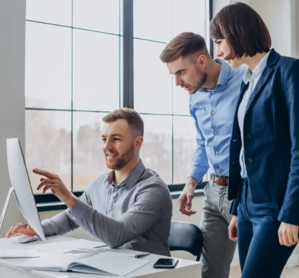 Trois collègues collaborent activement devant un ordinateur dans un bureau lumineux.