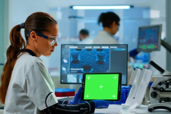 Chercheuse tenant une tablette à écran vert dans un laboratoire scientifique moderne.