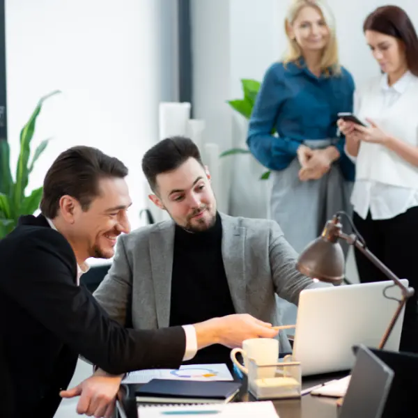Deux hommes d'affaires souriants collaborent sur un ordinateur dans un bureau moderne et animé.