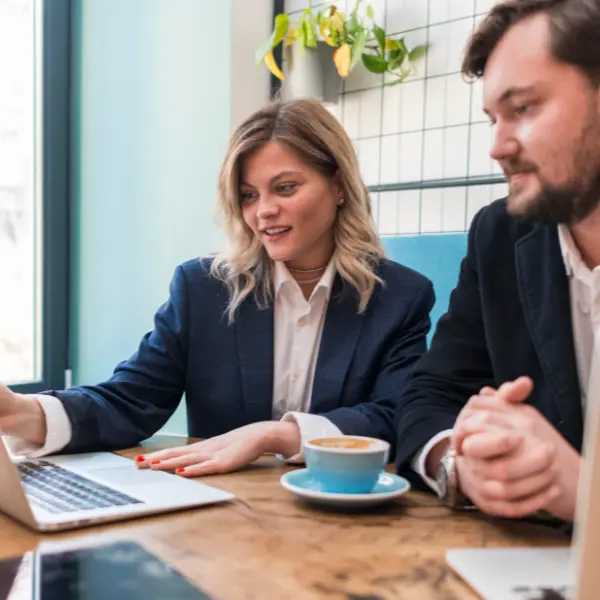 Deux collègues en veston collaborent sur un ordinateur portable dans un café lumineux.